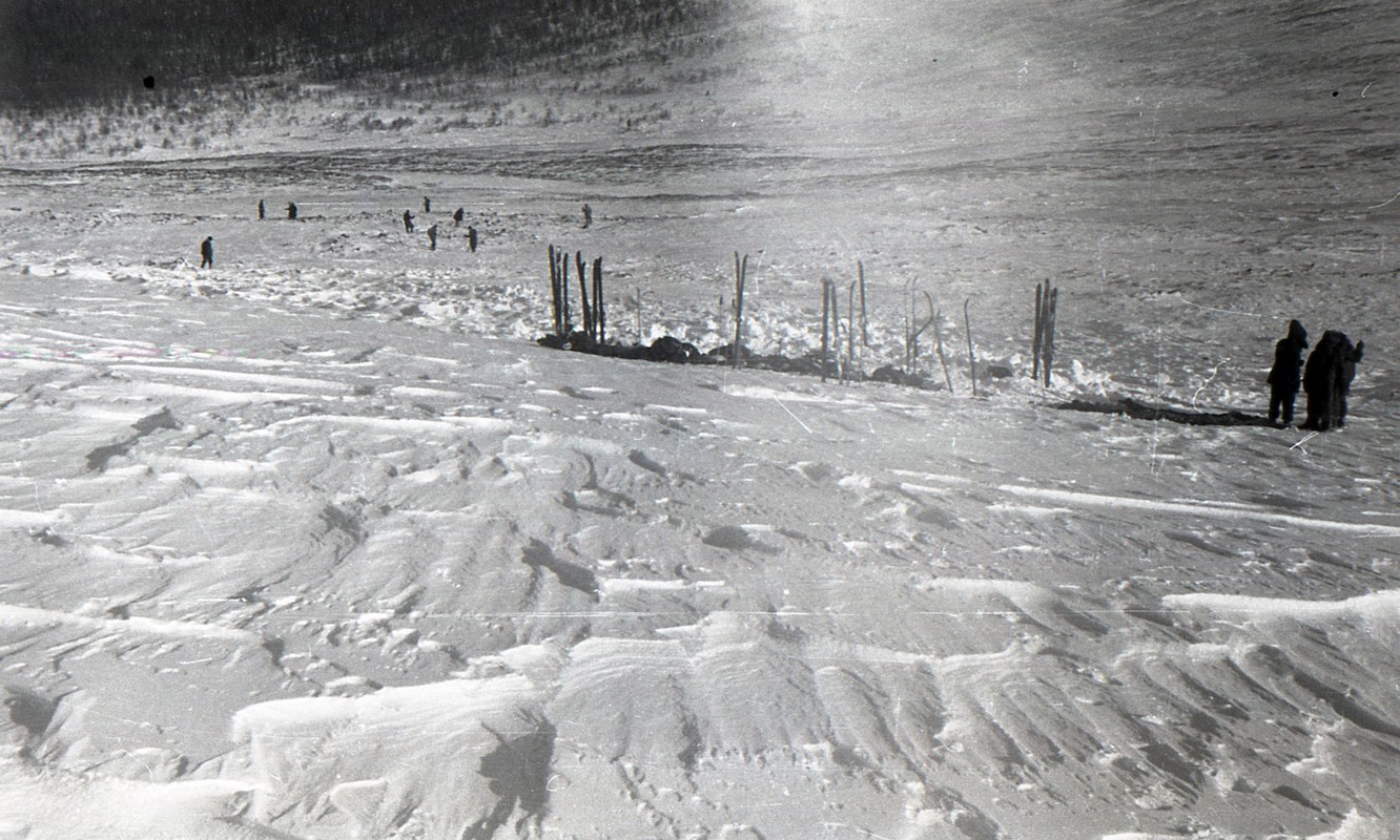 Dyatlov Pass: A scattered search team seen below clear patterns of heavily wind swept snow in the direction of the abandoned tent