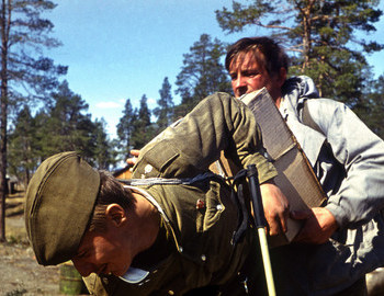 A soldier being helped to pick up the improvised backpack