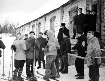 27 Jan 2959 - District 41, Lyuda is eating warm bread. Valya ties Zolotaryov's laces on a hooded windbreaker.
