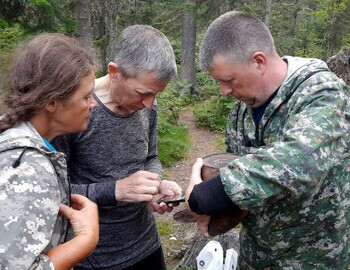Valentina Palkina, Shura Aleeksenkov and Sergey Ipatov examine an old tin can from stew found at the possible second location of the 1959 searcher's camp